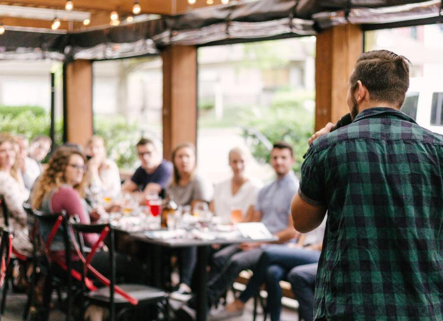 A speaker in front of a table with a small audience